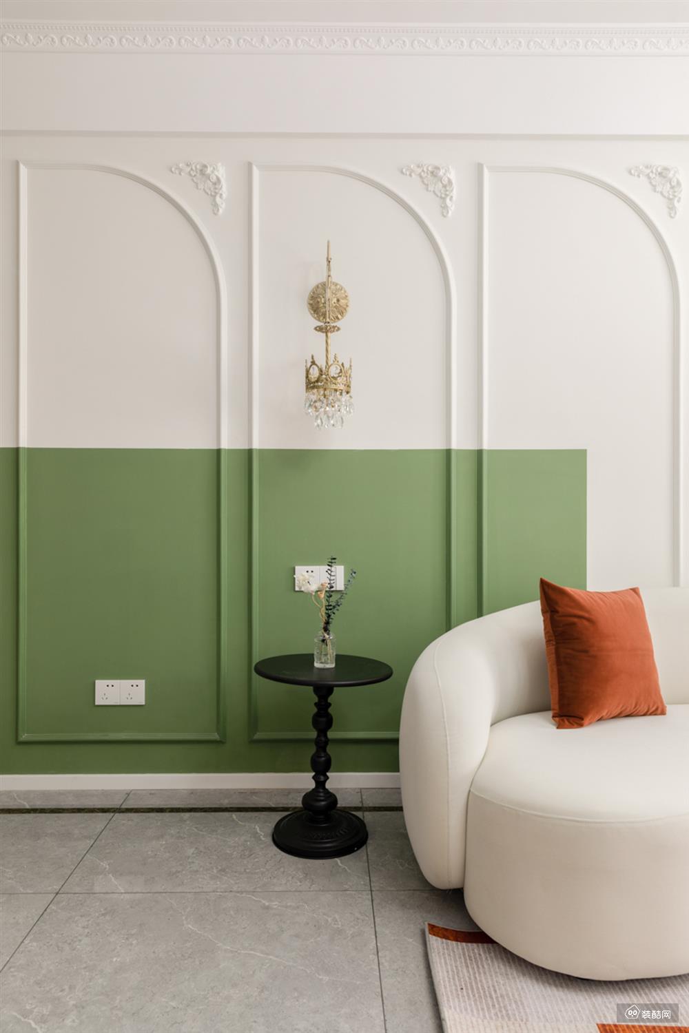 石膏线条+橄榄绿拼色半墙阵列式排开，丰富了空间层次，造就出雅致的空间韵律感。沙发旁放置了铁艺小边几，沉静的黑色带来恰到好处的平衡。