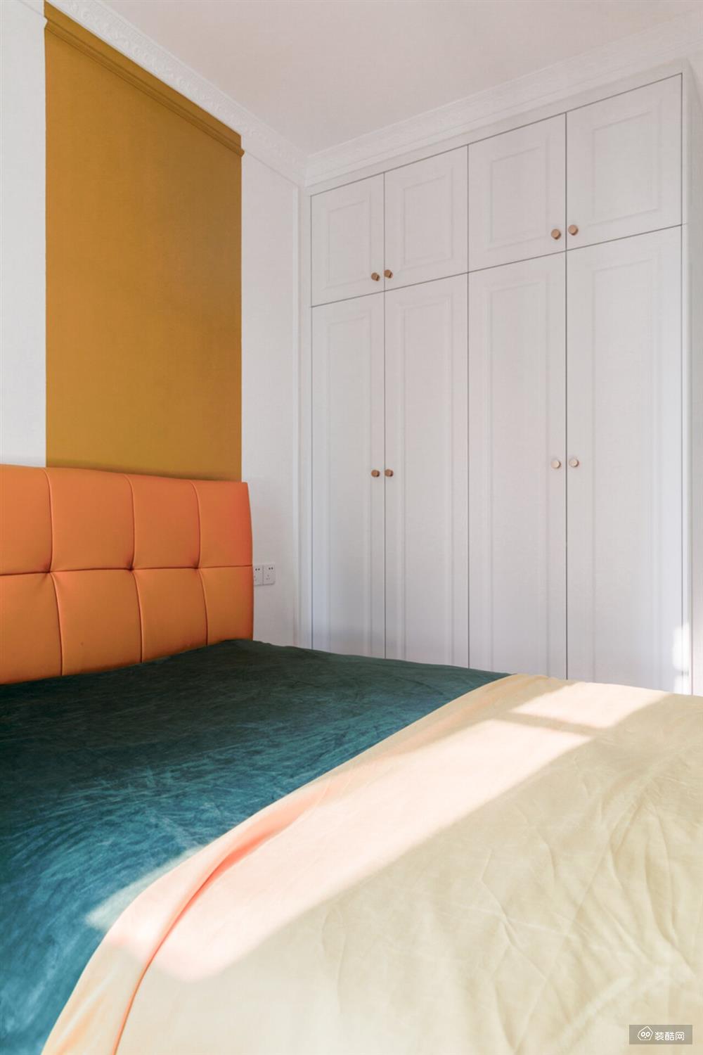 次卧墙面做了橙色块拼色设计，让墙面不再单调。同色系软包床背+拉扣工艺，大气舒适。白色衣柜上搭配了小巧圆润的黄铜拉手，显得俏皮可爱。